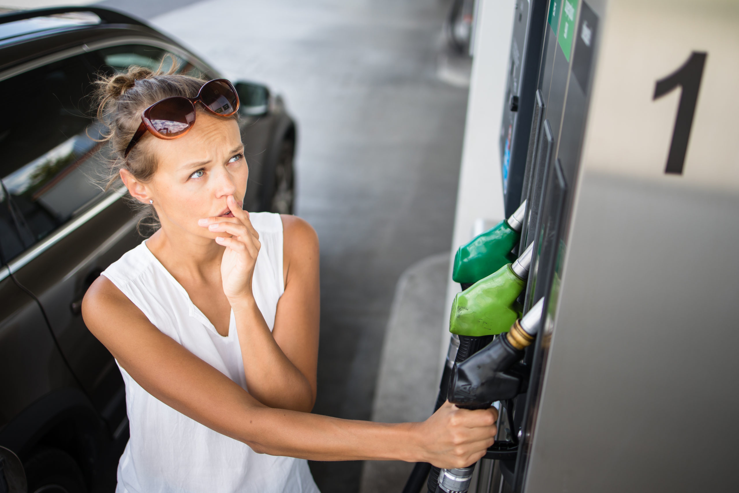 Young woman pumping gas at gas pump. Soaring gas prices concept.