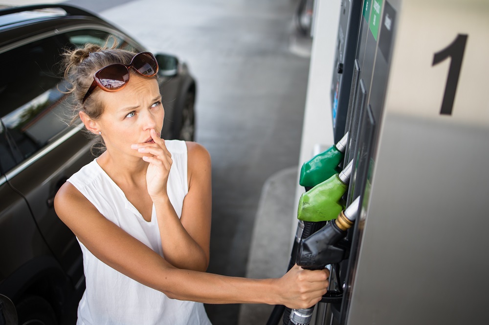Young woman pumping gas at gas pump. Soaring gas prices concept. Cheap Fuel tips.