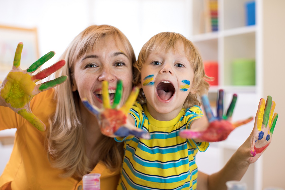 Cheerful Mother and son holding up painted hands smiling having fun with school holiday activities